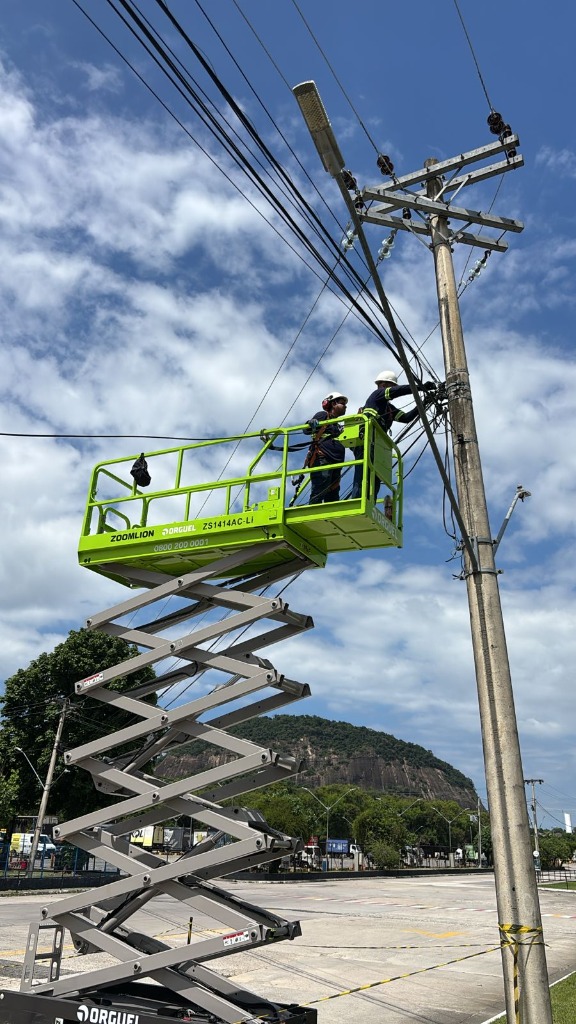 Dois técnicos equipados em uma plataforma elevatória realizando manutenção técnica em poste.