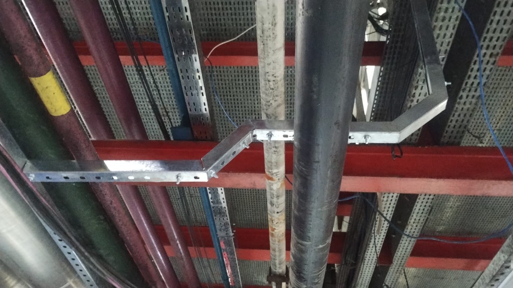 Eletrocalhas metálicas suspensas sob o teto de uma planta industrial.